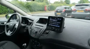 LCD screen of a DAB radio adapter for car displaying BBC station names and track info.