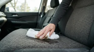 Parent using a cloth to wipe down durable waterproof car seat covers after a messy family day trip